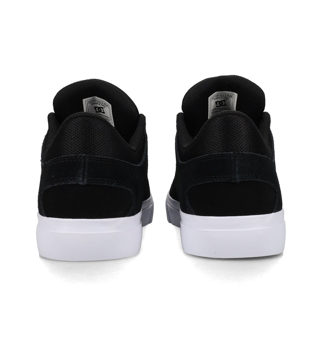 Back view of a pair of DC Shoes Men’s Onyx Shoes in black, featuring white soles. The sneakers are placed side by side, highlighting the heel, black mesh and suede textures, and a gray tag on each tongue. This minimal silhouette makes them an everyday go-to choice for both style and comfort.