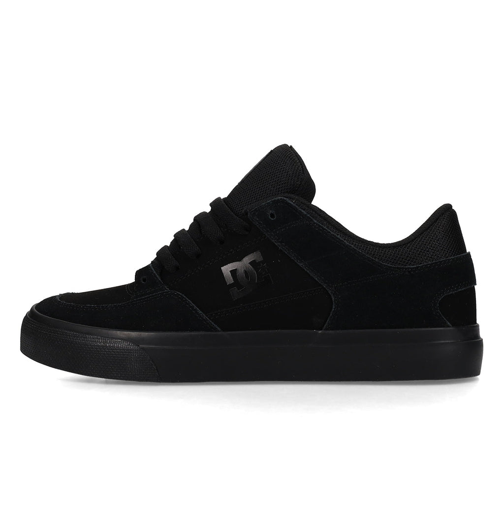 A black low-top skate shoe with a suede and mesh upper, black laces, a rubber sole, and the DC Shoes logo on the side.