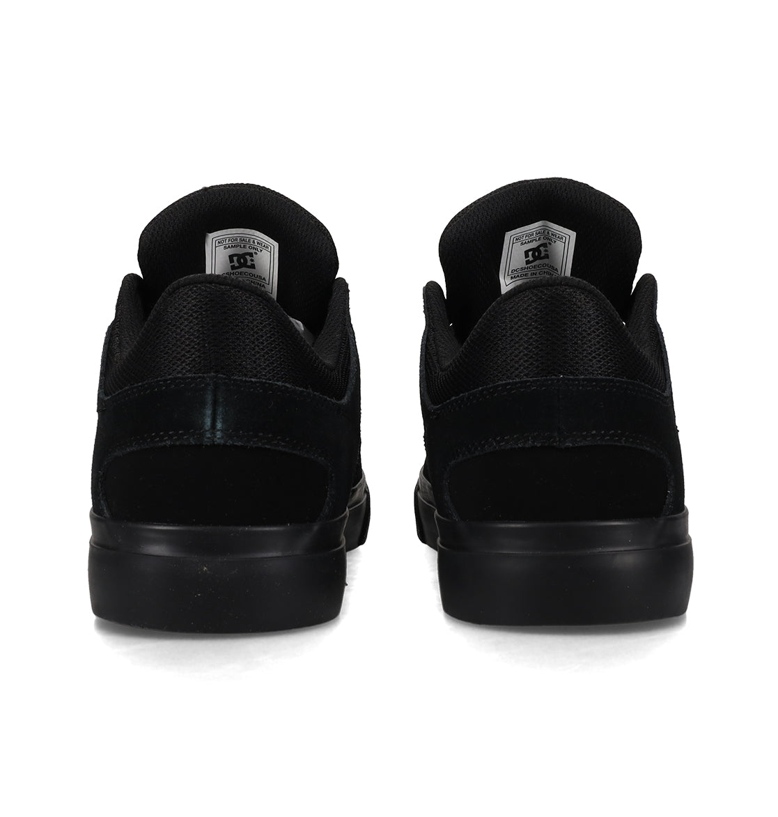 A pair of DC Shoes Men’s Onyx Shoes in black, shown from the back, showcases a minimal silhouette with matching black soles and a DC logo tag on each tongue—an everyday vulc style crafted for both comfort and style.