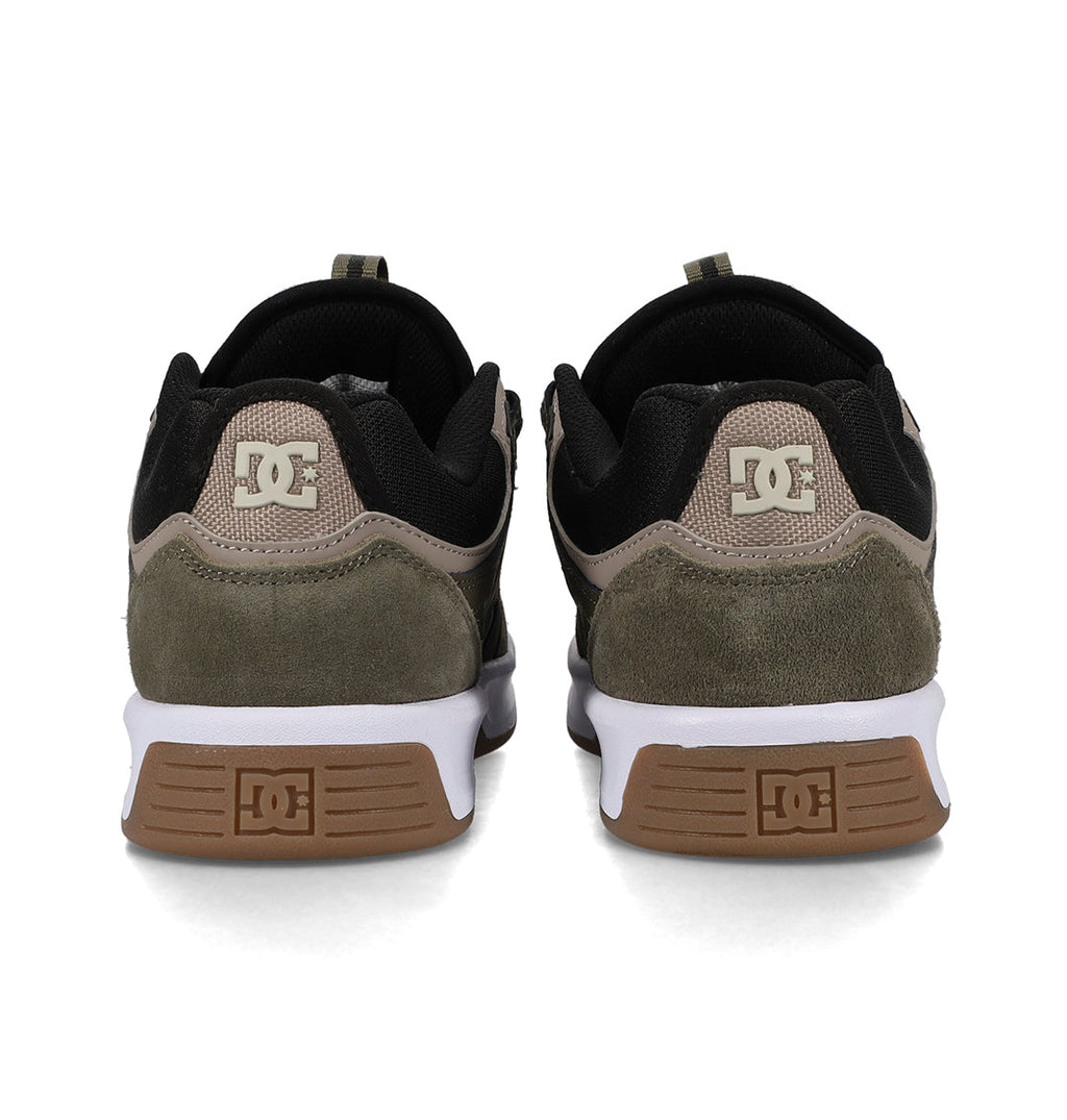 Back view of a pair of DC Shoes Men’s Kalynx Zero sneakers, featuring black, brown, and olive green panels, white midsoles, and brown outsoles. The DC logo appears on the heel and sole of each shoe.