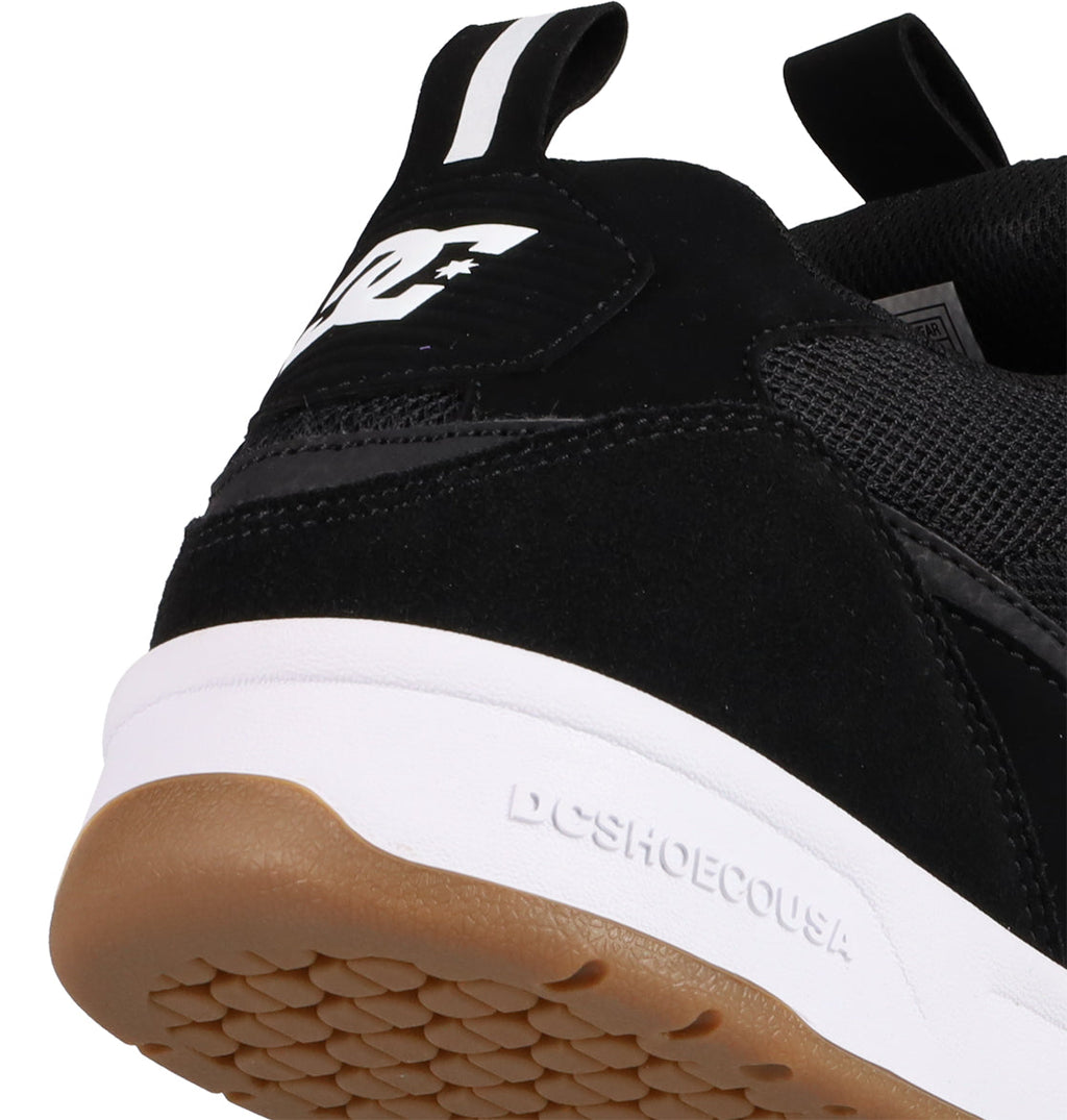 Close-up of the heel of a black DC Shoes Men's JS-2 Shanahan Pro Skate Shoe with white sole and gum outsole. This John Shanahan-inspired design shows the DC logo on the side and DCSHOECOUSA embossed on the midsole.