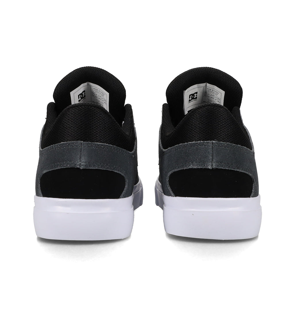 Back view of a pair of Men’s Onyx Skate Shoes by DC Shoes in black and grey, showcasing fabric and suede accents with white soles in a minimal silhouette. The DC Shoes logo is displayed on the inside tongue labels, emphasizing the sleek design inspired by the iconic Onyx vulc style.