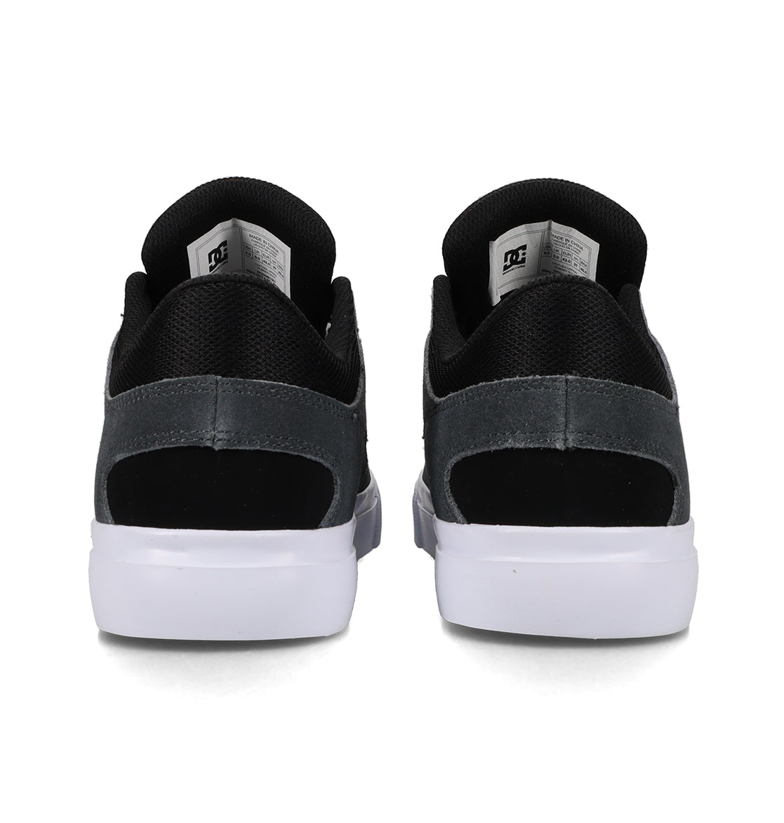 Back view of a pair of Men’s Onyx Skate Shoes by DC Shoes in black and grey, showcasing fabric and suede accents with white soles in a minimal silhouette. The DC Shoes logo is displayed on the inside tongue labels, emphasizing the sleek design inspired by the iconic Onyx vulc style.