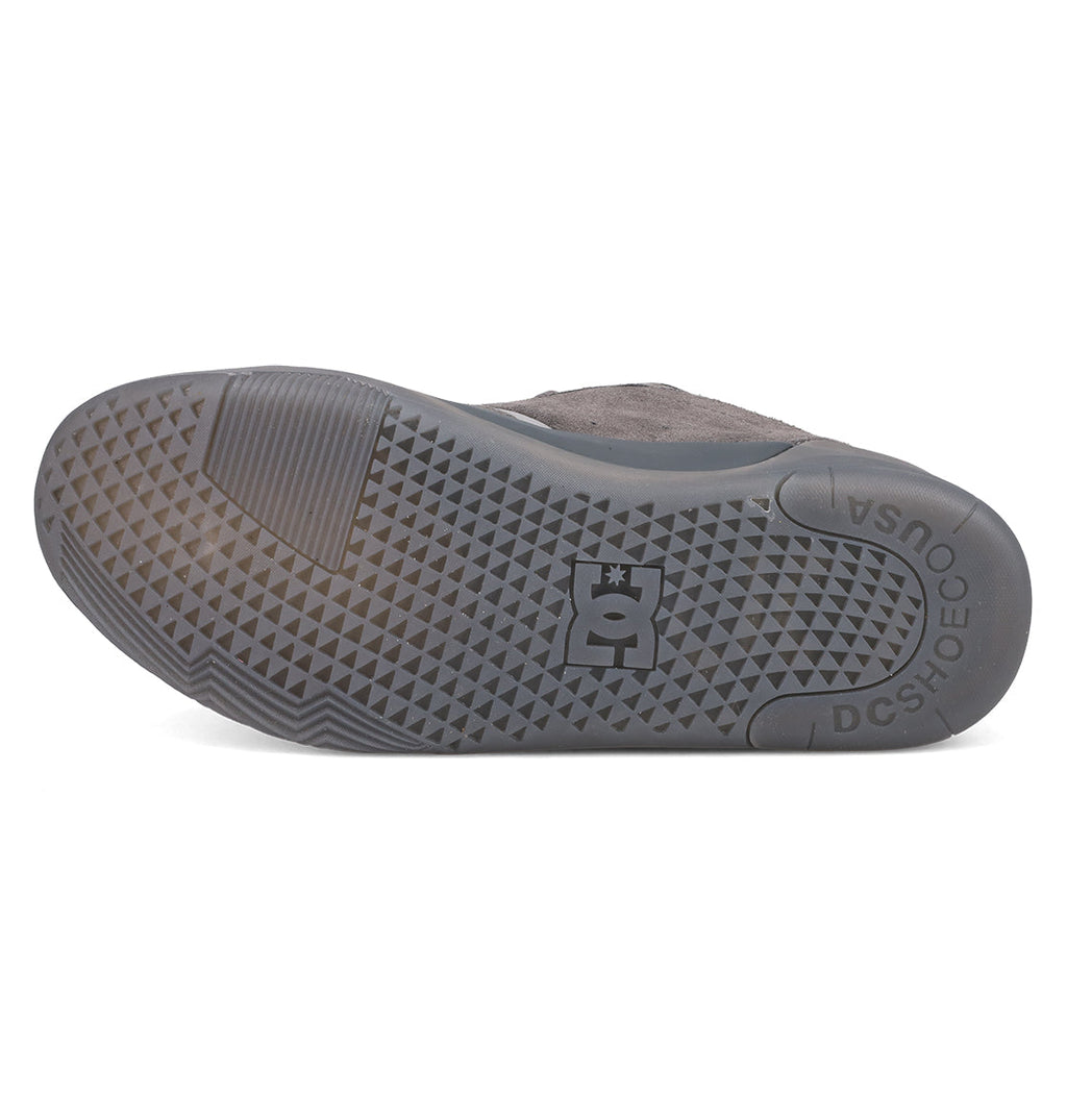The image displays the sole of a grey DC Shoes Men's Fractal SE, featuring a textured triangular tread and the DC logo at the center. "DC SHOES" and "QUUSA" are molded into this street-inspired sneaker’s sole near the heel.