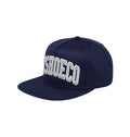 The University Cap Snapback by DC Shoes is an estate blue, flat-brim hat designed in true streetwear style. It features bold white embroidered SHOECO lettering across the front, stitched eyelets, a top button, and classic snapback detailing.