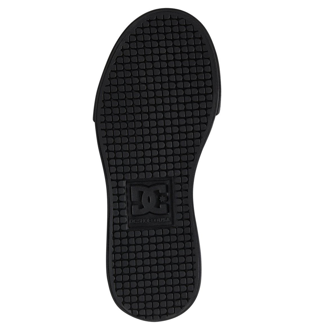Black sole of the Kids’ Pure Shoes by DC Shoes, featuring a textured, grid-like tread pattern and a raised rectangular DC Shoes logo in the center. Designed for durability, the sole is shown from the bottom against a white background.