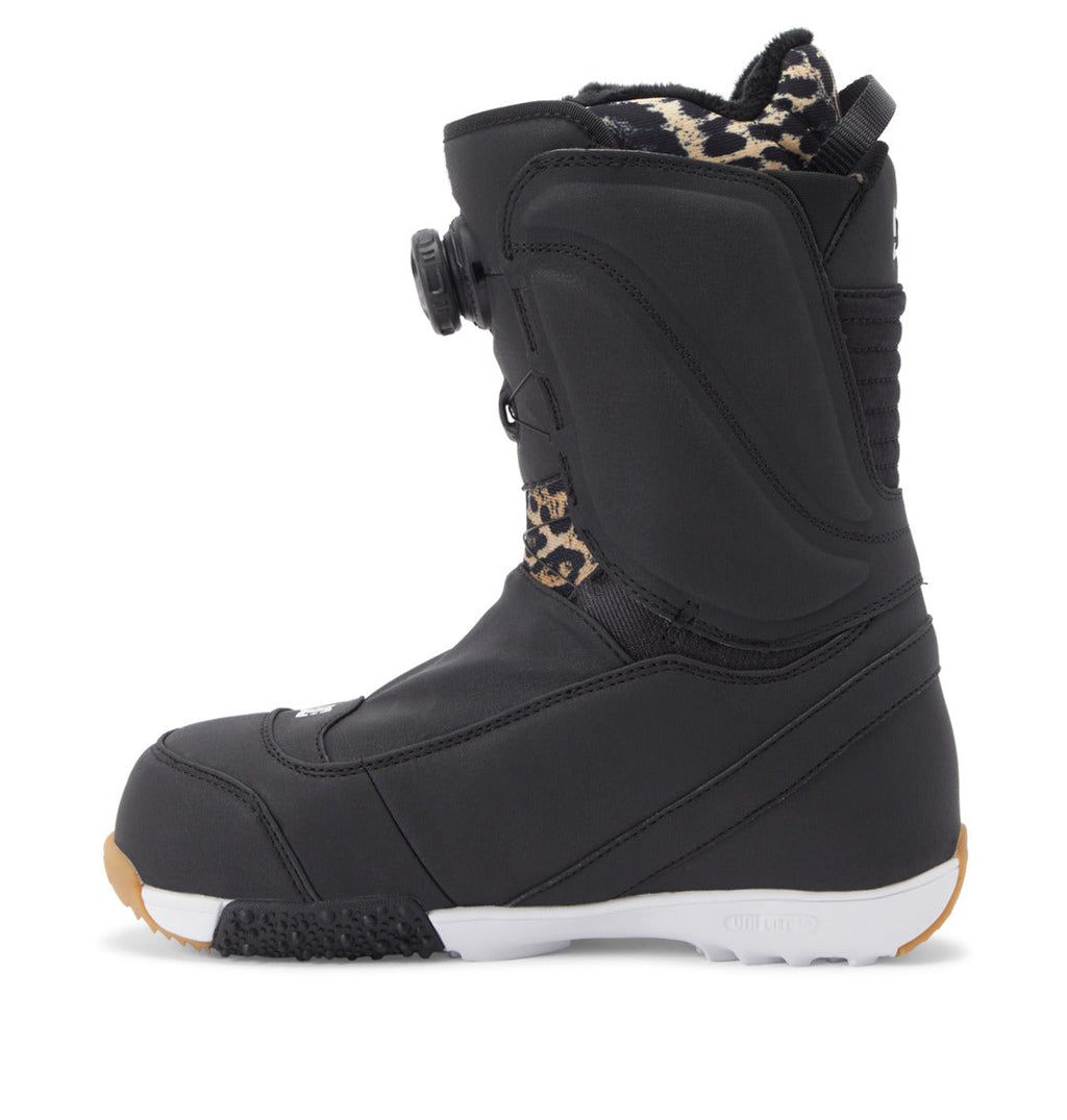 A black Women’s Mora BOA® Snowboard Boot by DC Shoes features a white sole, tan tread, and leopard print lining. The boot is equipped with the BOA Fit System dial closure and visible stitching details, while PrimaLoft insulation provides warmth and comfort on the slopes.