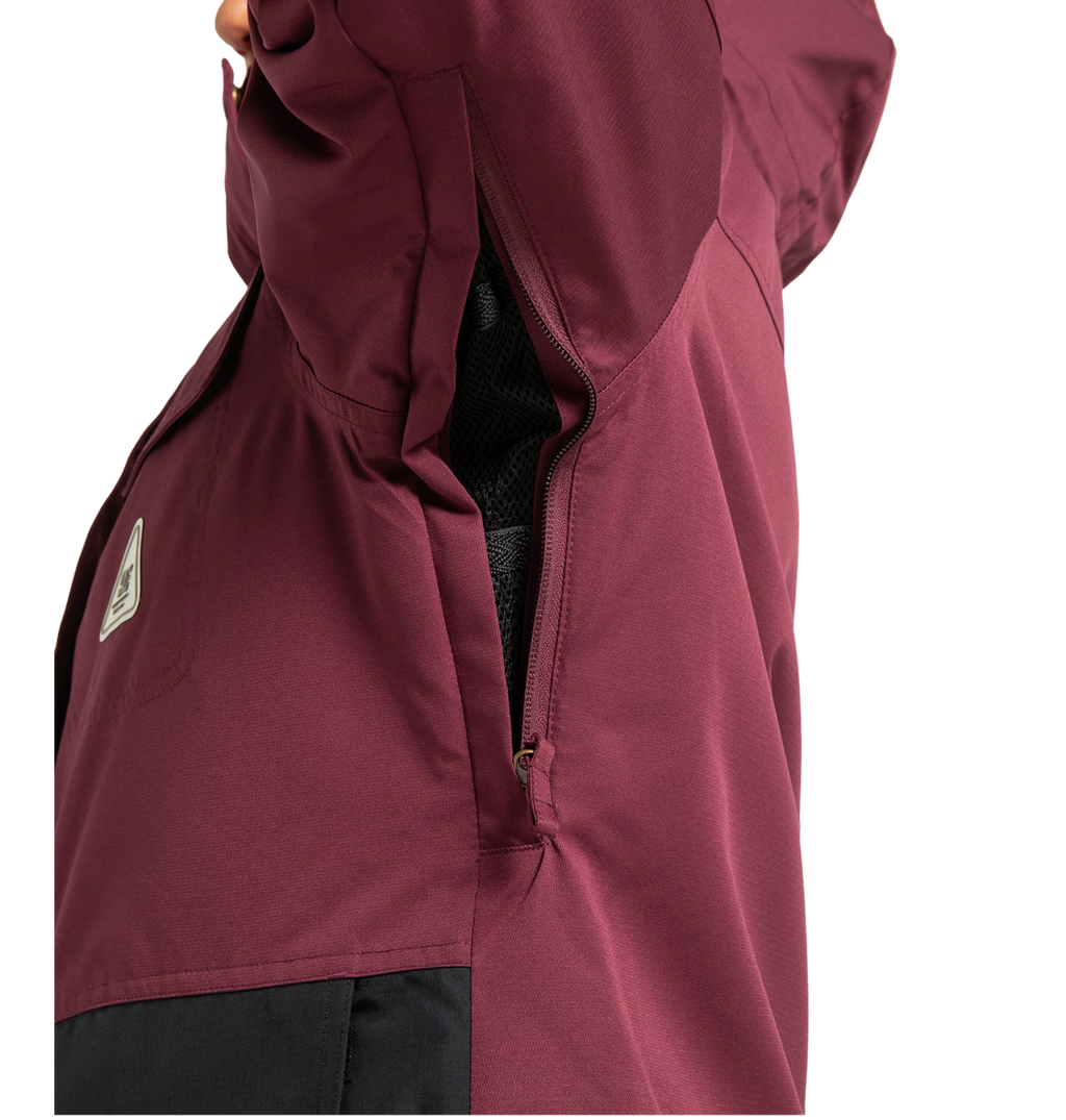 A close-up of the DC Shoes Women’s Liberate Insulated Jacket in burgundy with a black panel, highlighting a partially open zippered underarm vent and visible mesh lining—offering ideal protection for your next winter adventure.