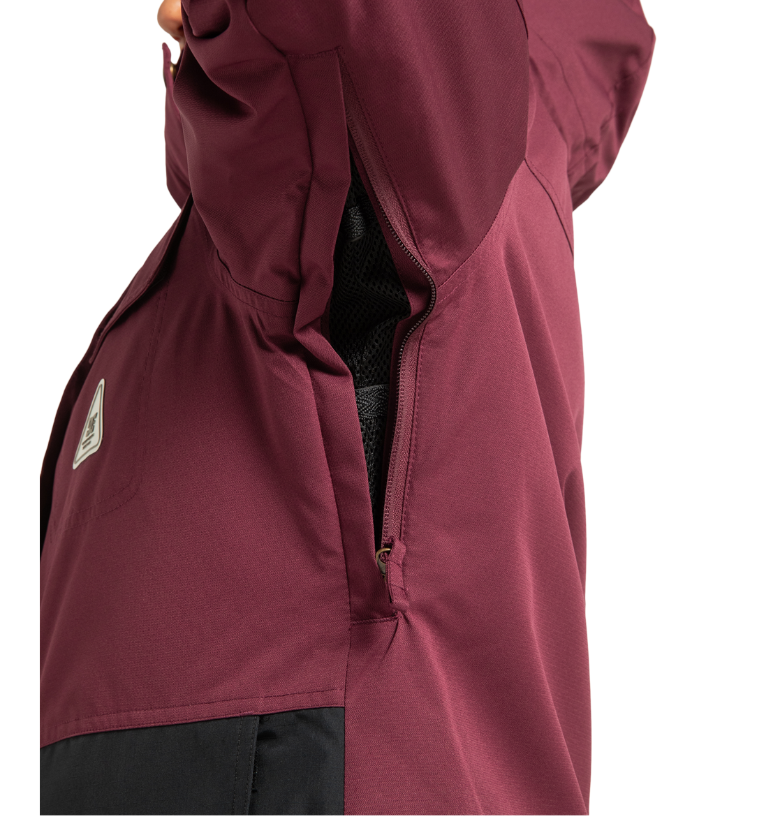 A close-up of the DC Shoes Women’s Liberate Insulated Jacket in burgundy with a black panel, highlighting a partially open zippered underarm vent and visible mesh lining—offering ideal protection for your next winter adventure.