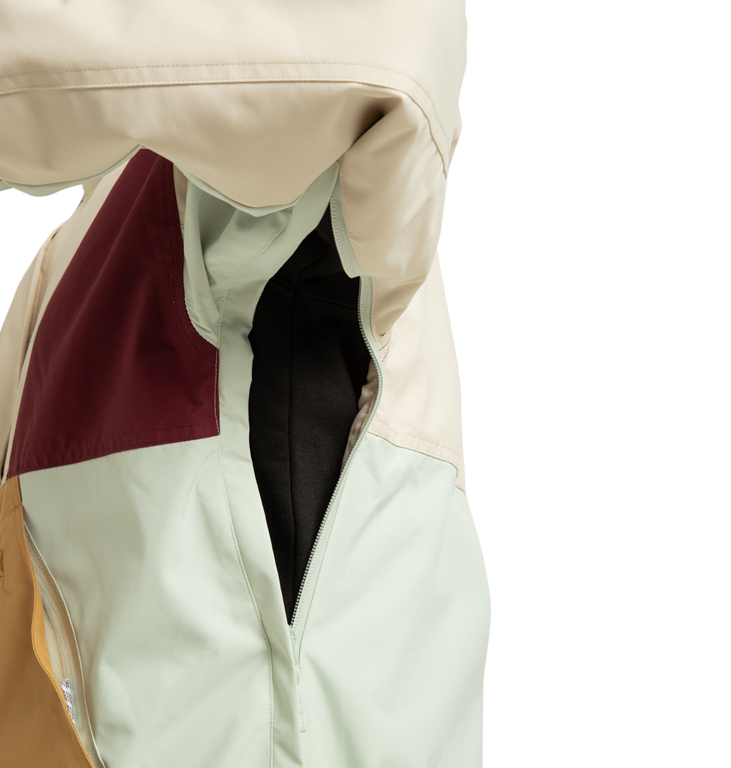 Close-up of the DC Shoes Women’s Chalet Anorak Insulated Jacket, color-blocked in cream, mint green, mustard yellow, and burgundy panels. This outdoor adventure jacket features a zippered underarm vent, shown open to reveal black fabric inside the sleeve.