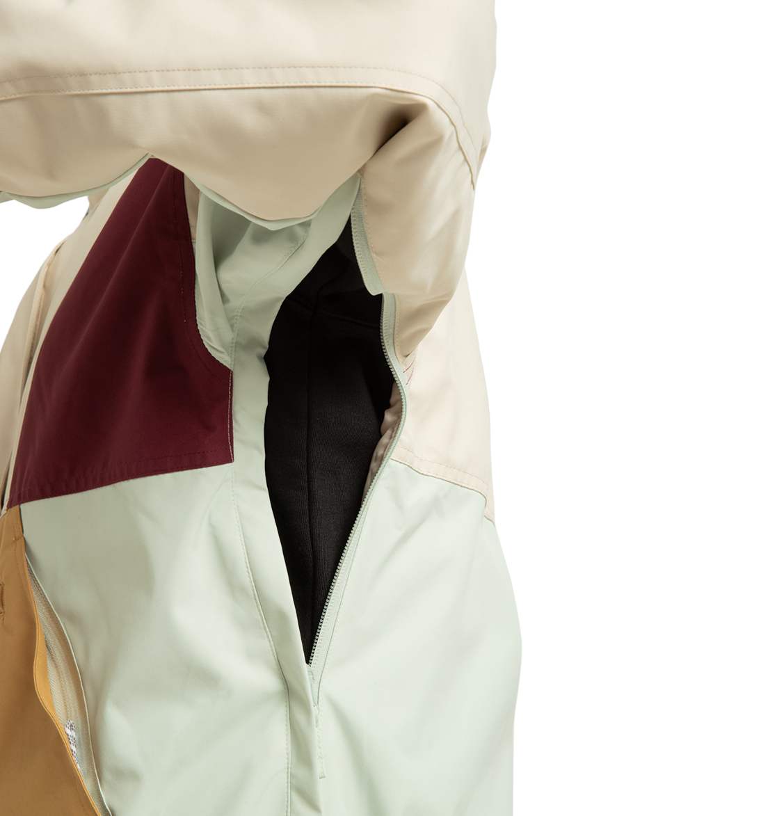 Close-up of the DC Shoes Women’s Chalet Anorak Insulated Jacket, color-blocked in cream, mint green, mustard yellow, and burgundy panels. This outdoor adventure jacket features a zippered underarm vent, shown open to reveal black fabric inside the sleeve.