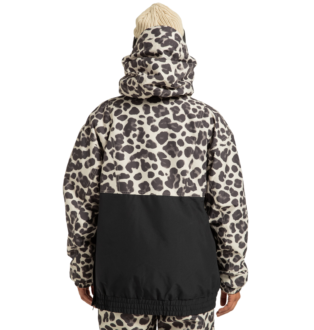 A person is shown from the back against a plain white background, wearing the DC Shoes Women’s Chalet Anorak Insulated Jacket featuring an animal print with a black lower half and a hood, paired with matching pants and a cream knit hat.