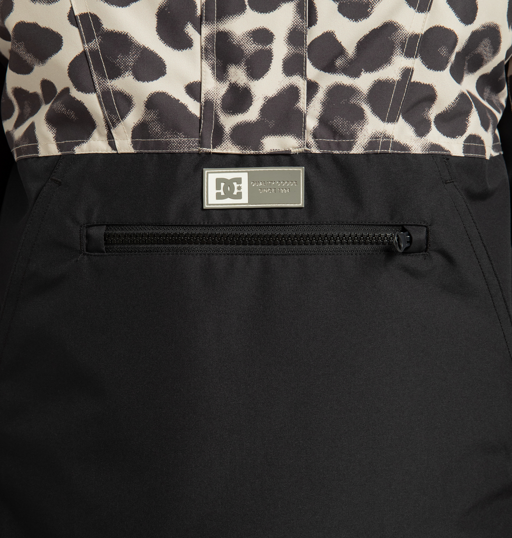Close-up of the DC Shoes Women’s Chalet Anorak Insulated Jacket, featuring a black lower section, leopard print upper section, zippered pocket, and a small rectangular DC Shoes logo patch above the zipper. Made from recycled polyester for an eco-friendly touch.