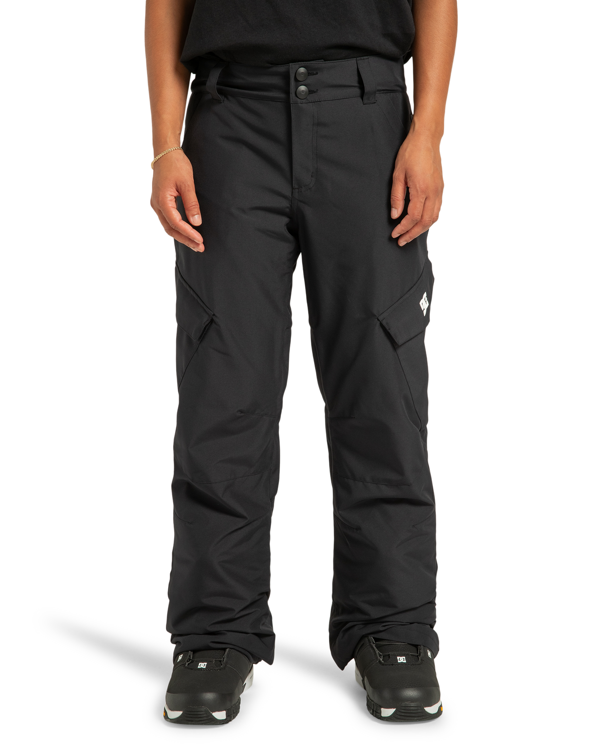 A person is shown wearing DC Shoes Women’s Nonchalant Insulated Snow Pants in black and black sneakers, standing against a white background. Their upper body is partially visible, with hands relaxed by their sides.