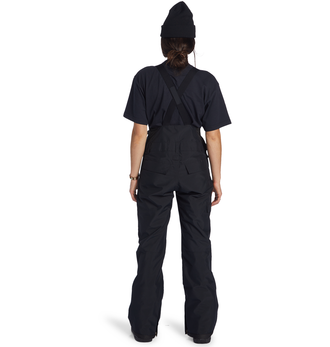 A person wearing the DC Shoes Women’s Valiant Bib, a black t-shirt, and a black beanie stands facing away against a plain white background.