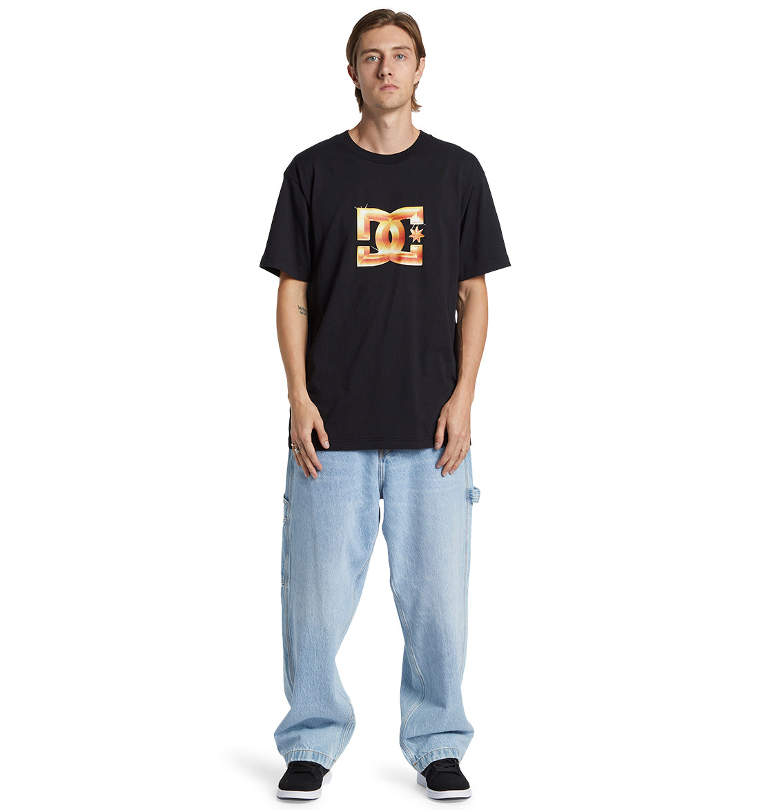 A person wearing a black DC Shoes logo t-shirt, Men’s Worker Baggy Carpenter Ril Jeans from DC Shoes in light blue, and black shoes stands facing forward against a plain white background.