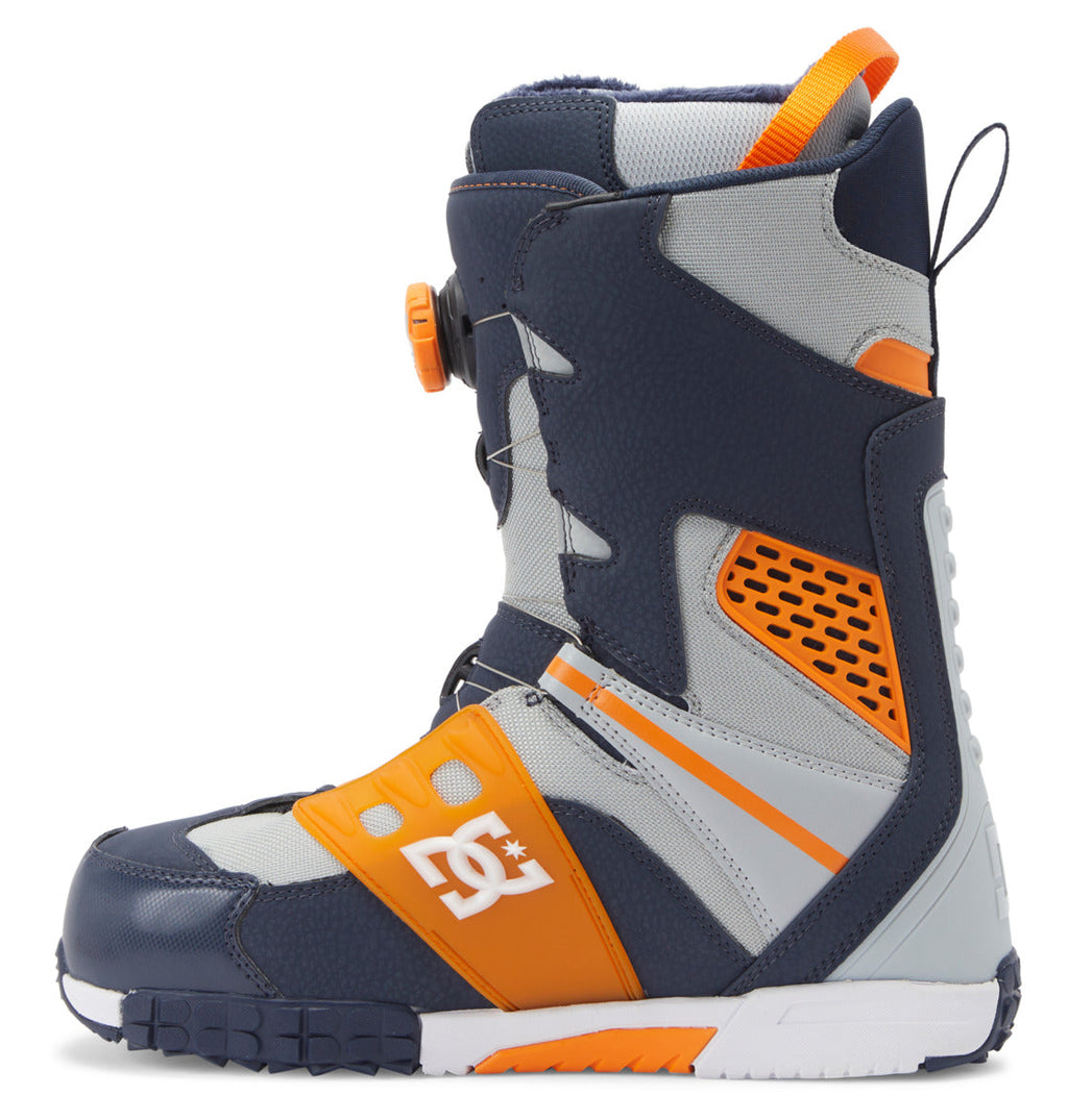 The Men’s Phantom BOA® Snowboard Boots by DC Shoes feature a navy blue, orange, and gray design with a textured sole, orange accents, and a white DC logo on the side. These boots offer a high ankle silhouette, PrimaLoft insulation for extra warmth, and a convenient pull loop at the back.