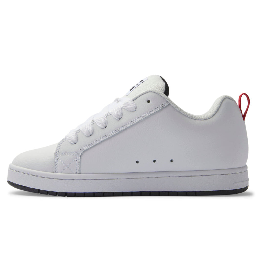 Showcased in a sleek side profile view, the DC Shoes Men’s Court Graffik Shoes feature a white low-top design with white laces, a distinctive two-tone sole with black accents, and a small red pull tab on the heel.