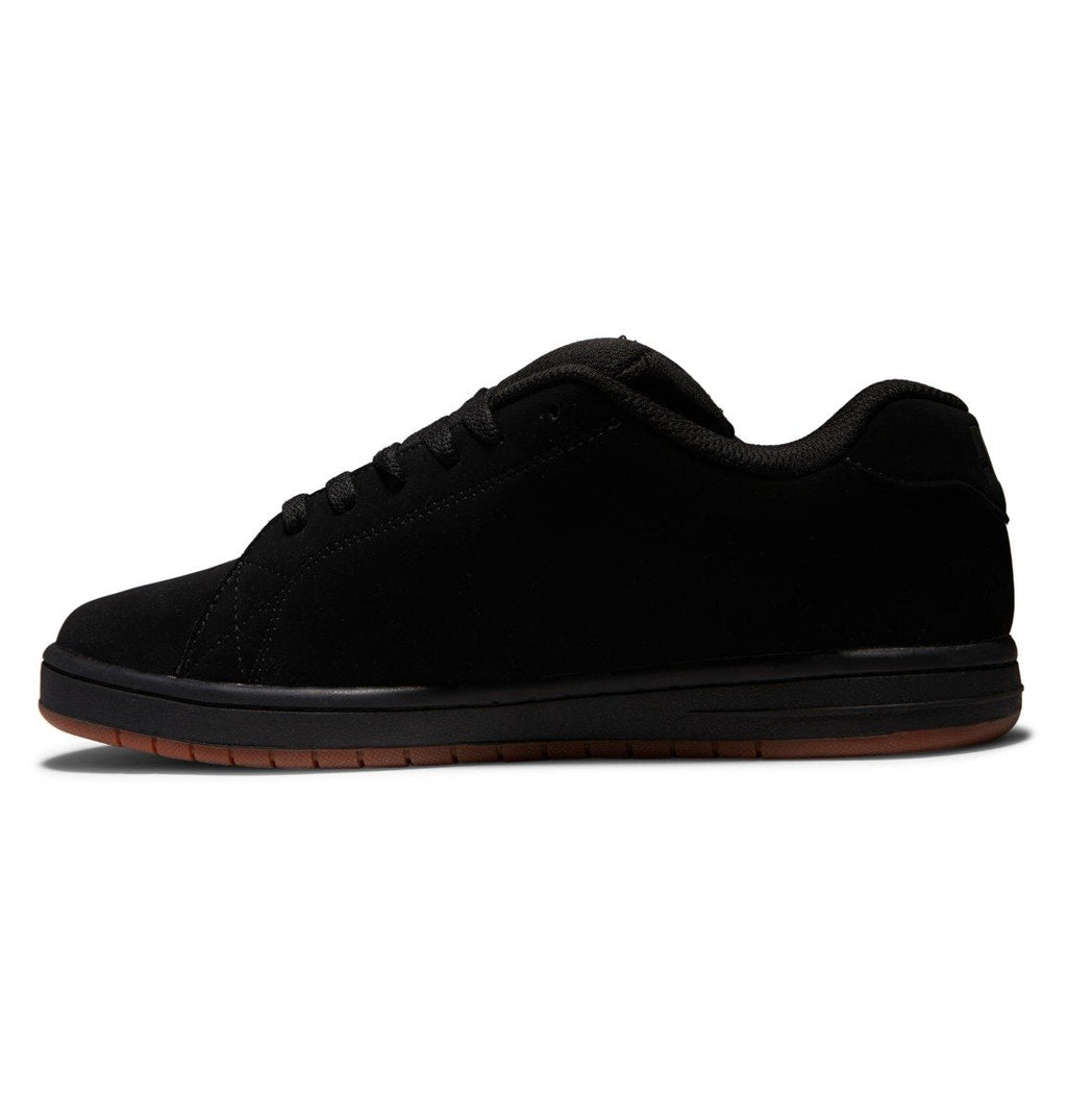 A side-profile view displays the Men’s Gaveler Shoes by DC Shoes in black, featuring a low-top silhouette with a suede finish and matching black laces. Designed for style and comfort, these chunky-inspired sneakers are set on a dark brown rubber sole against a white background.