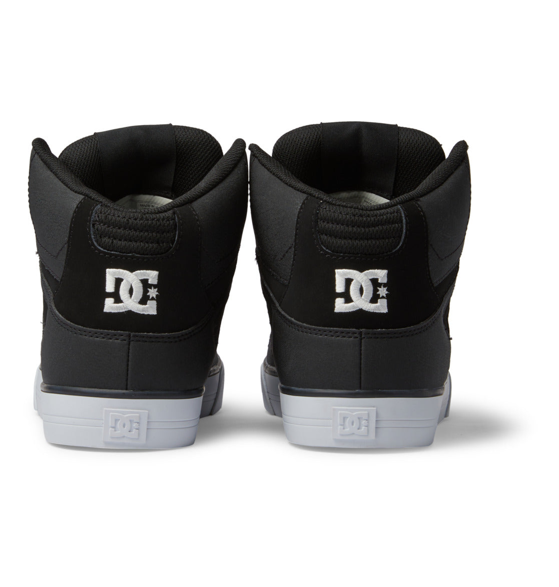 Rear view of a pair of DC Shoes Men’s Pure High-Top Shoes in black, featuring a white embroidered DC logo on the heel and white rubber soles—combining durability and comfort in a stylish design—displayed against a white background.