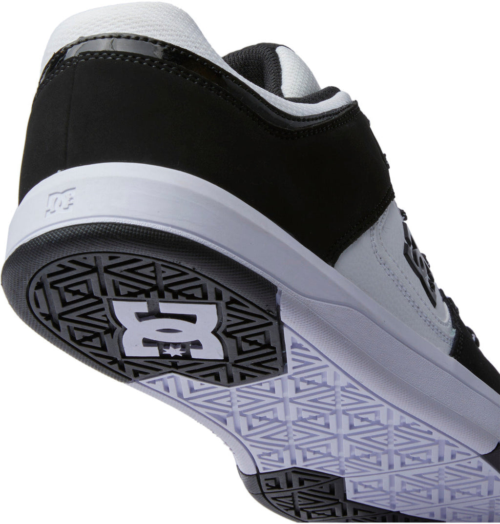 A close-up of the Men’s DC Cure Shoes by DC Shoes in black and white, viewed from the rear and bottom, highlights the textured sole prominently featuring the DC Shoes logo. The leather upper enhances durability and style, making these shoes ideal for everyday wear.