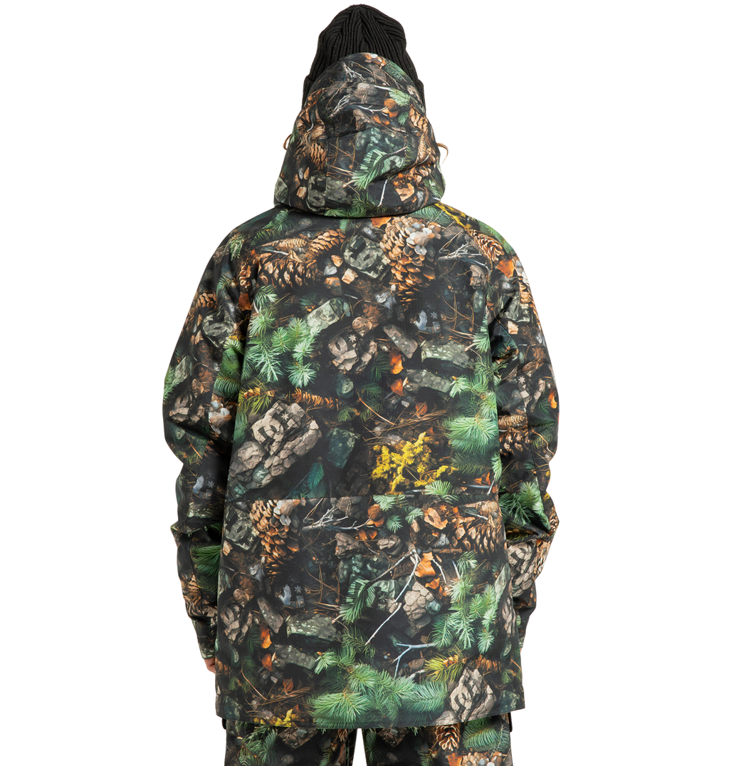 A person wearing the DC Shoes Men’s Tundra Insulated Jacket, featuring an eco-friendly design with a forest camouflage pattern of pinecones, leaves, and green foliage, stands facing away from the camera against a plain white background.