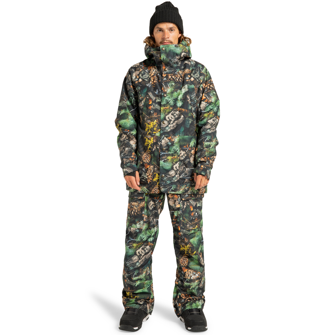 A person is standing facing forward against a plain white background, wearing a matching camouflage-patterned DC Shoes Men’s Tundra Insulated Jacket and pants, paired with a black beanie and black boots.