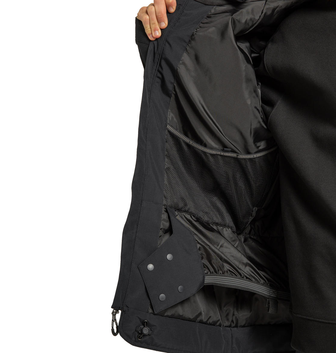A person holds open a DC Shoes Men’s Tundra Insulated Jacket in black, revealing the inside lining, mesh pockets, and snap buttons. Only the person’s hand and part of their torso are visible.
