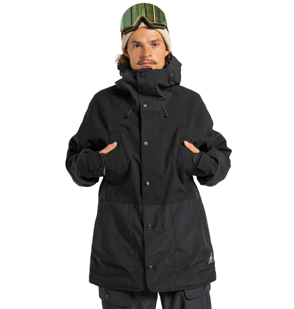 A person wearing the DC Shoes Men’s Tundra Insulated Jacket in black, paired with black pants and ski goggles, stands facing forward with hands in the jacket’s chest-high pockets against a plain white background.
