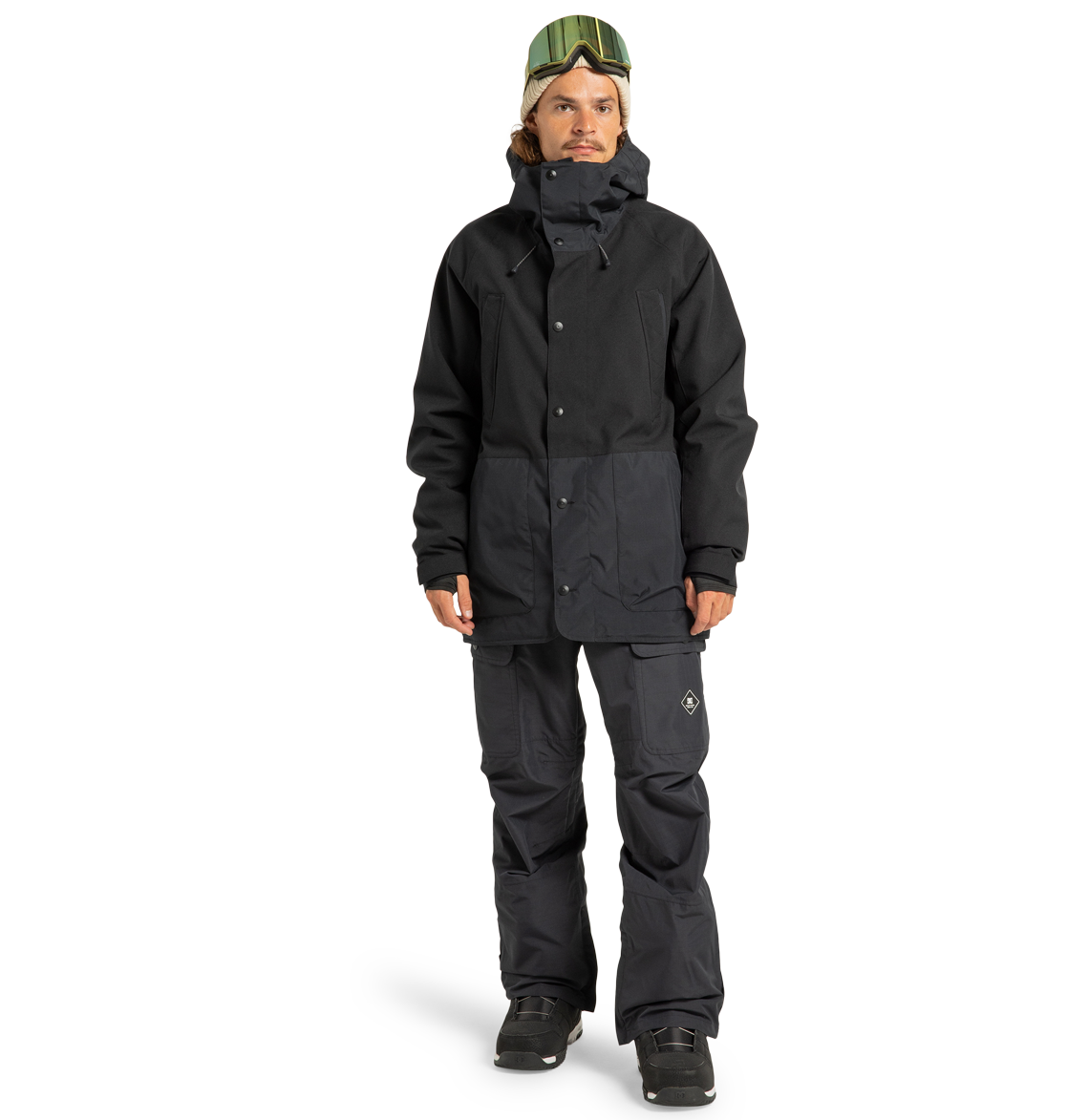 A person is wearing the DC Shoes Men’s Tundra Insulated Jacket and pants, black boots, and green ski goggles, standing against a plain white background. The insulated jacket offers exceptional warmth while adding a stylish edge to the overall look.