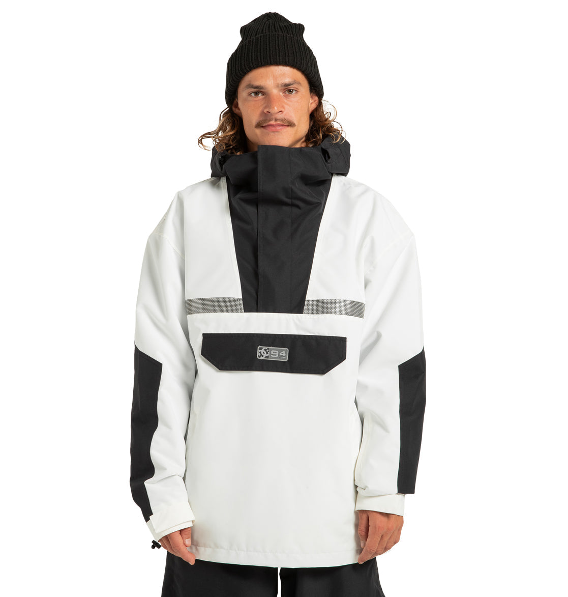 A person wearing a black beanie and the DC Shoes Men’s DC-43 Anorak Jacket—a white and black hooded winter coat featuring a front pocket, reflective strip, and made from recycled polyester—stands against a plain white background.