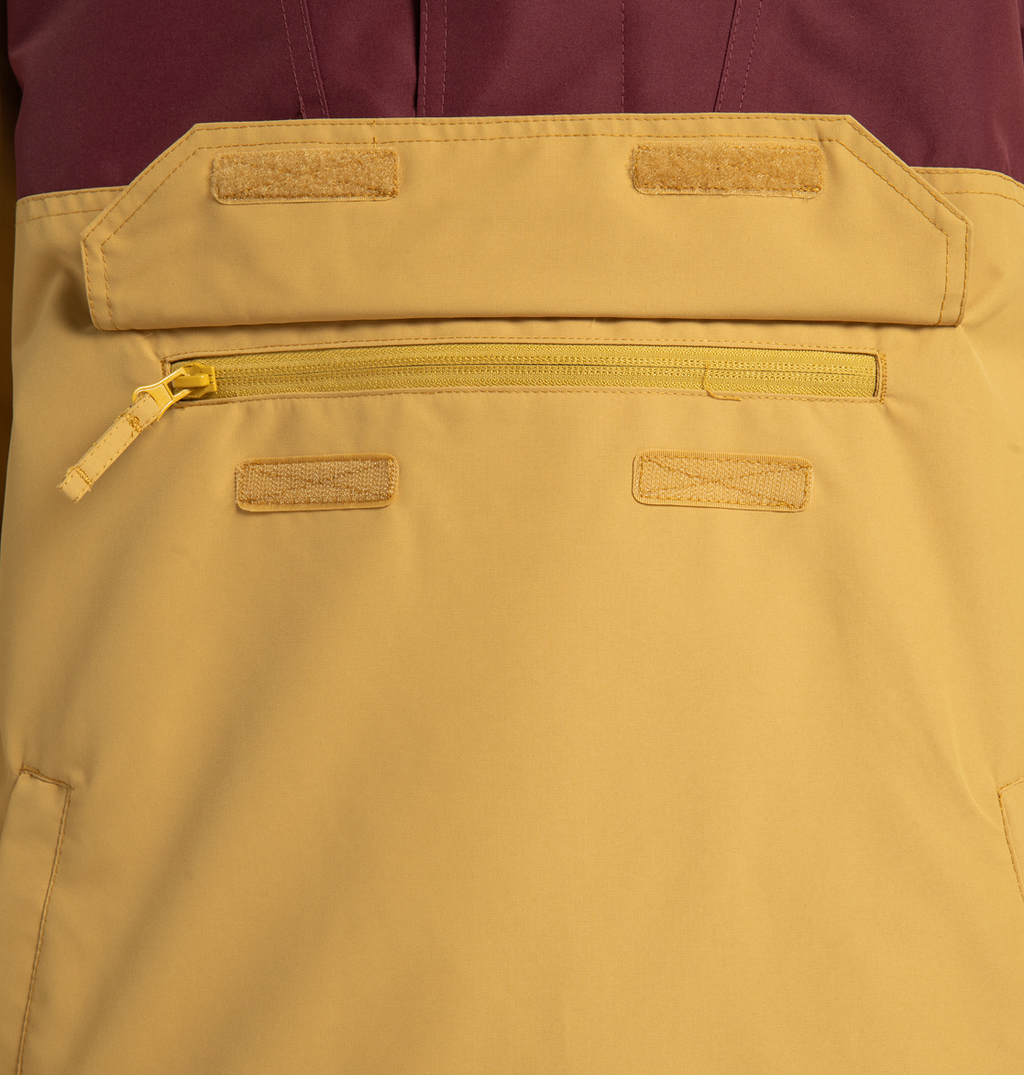 Close-up of ski bib pants featuring a yellow zippered pocket, Velcro attachment points, and a striking gold and burgundy two-tone colorblock design—crafted to perfectly complement the Men’s DC-43 Anorak Shell Jacket from DC Shoes or your favorite recycled polyester jacket.