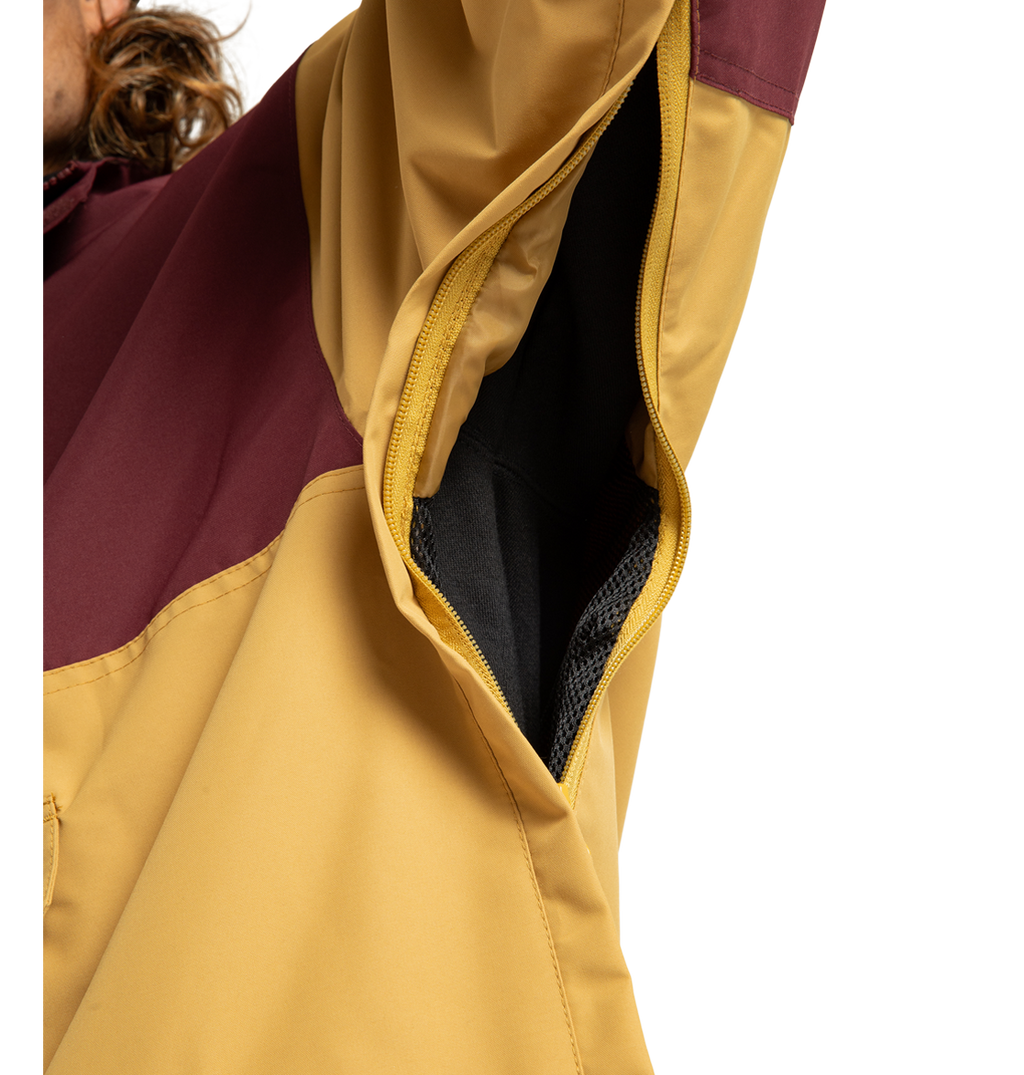 Close-up of the Men’s DC-43 Anorak Shell Jacket by DC Shoes, focusing on its zippered armpit vent that reveals the interior mesh lining. The jacket features a yellow color with a maroon upper sleeve section, and the zipper is partially open.