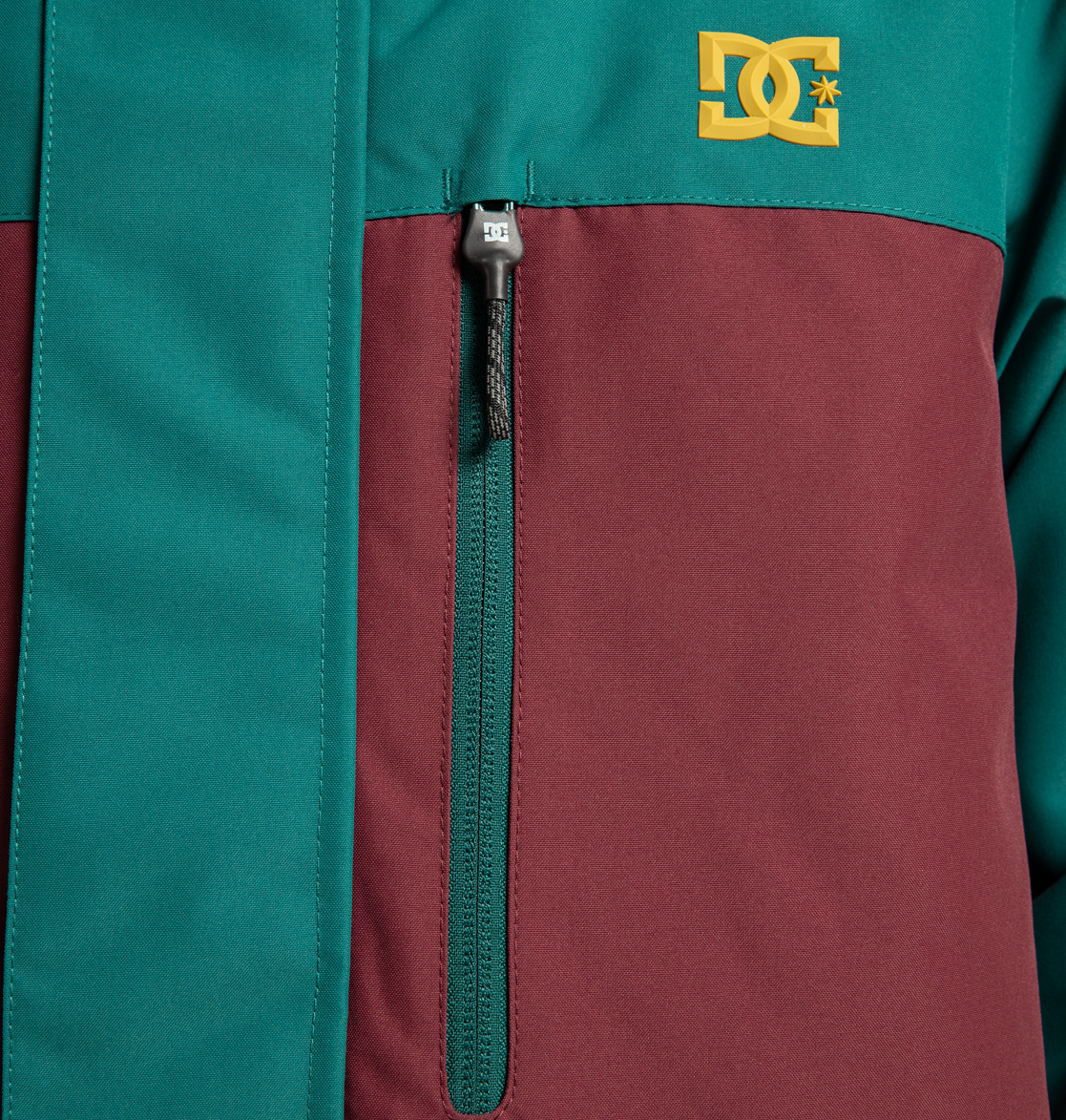 Check out the Men’s Defiant Insulated Jacket from DC Shoes, shown here in a teal and burgundy colorblock design made from recycled polyester. This winter-ready jacket features a zippered chest pocket and is finished with a gold embroidered DC Shoes logo—your ideal companion for any cold-weather adventure.
