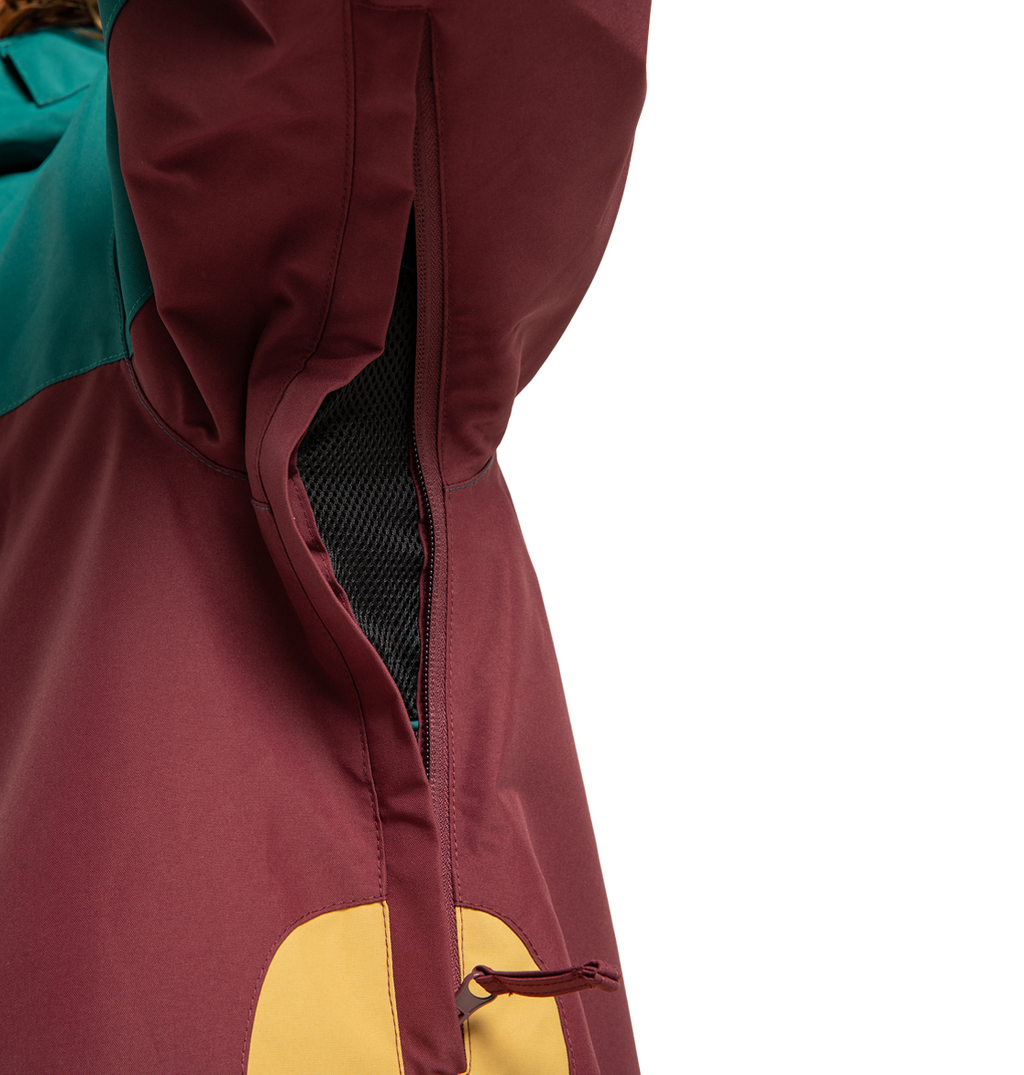 Close-up of the Men’s Defiant Insulated Jacket by DC Shoes, featuring burgundy, teal, and yellow panels with an open zippered vent lined in black mesh. Made from recycled polyester, this jacket keeps you comfortable and stylish on any winter adventure.