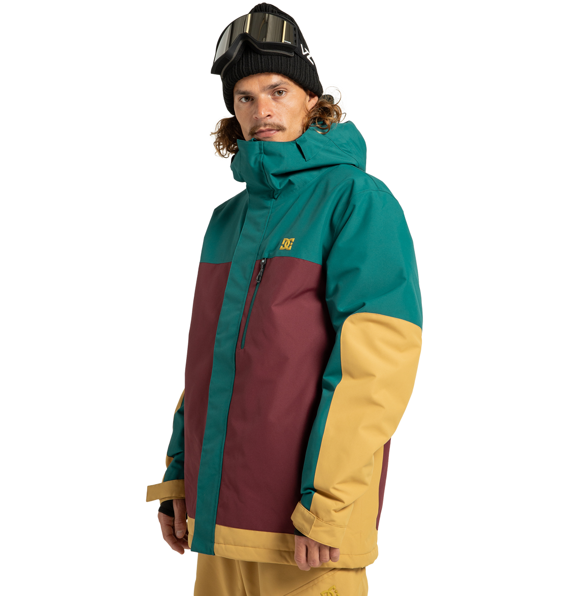 A man wearing the DC Shoes Men’s Defiant Insulated Jacket in teal, maroon, and yellow—crafted from recycled polyester—paired with matching yellow pants and a black beanie topped with ski goggles, stands against a plain white background, ready for any winter adventure.