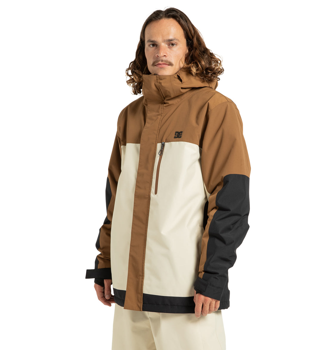 A person with long hair wears the DC Shoes Men’s Defiant Insulated Snow Jacket in a tricolor design of brown, cream, and black, featuring a hood and zippered chest pocket, standing against a plain white background.