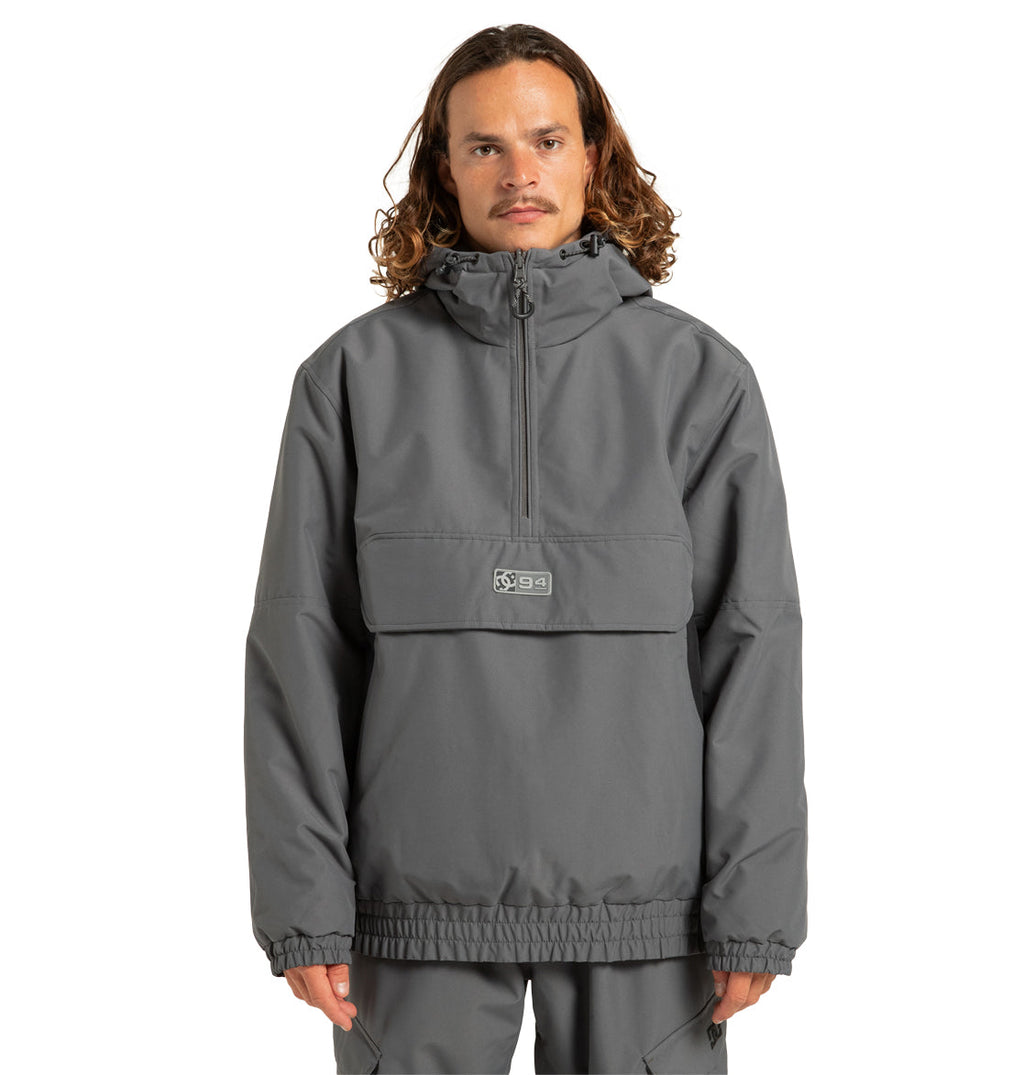 A person with wavy, shoulder-length hair wears the DC Shoes Unisex Nexus Reversible Insulated Anorak Jacket in gray—featuring a weather-resistant shell, half-zip design, front flap pocket, and elastic cuffs—standing against a plain white background.