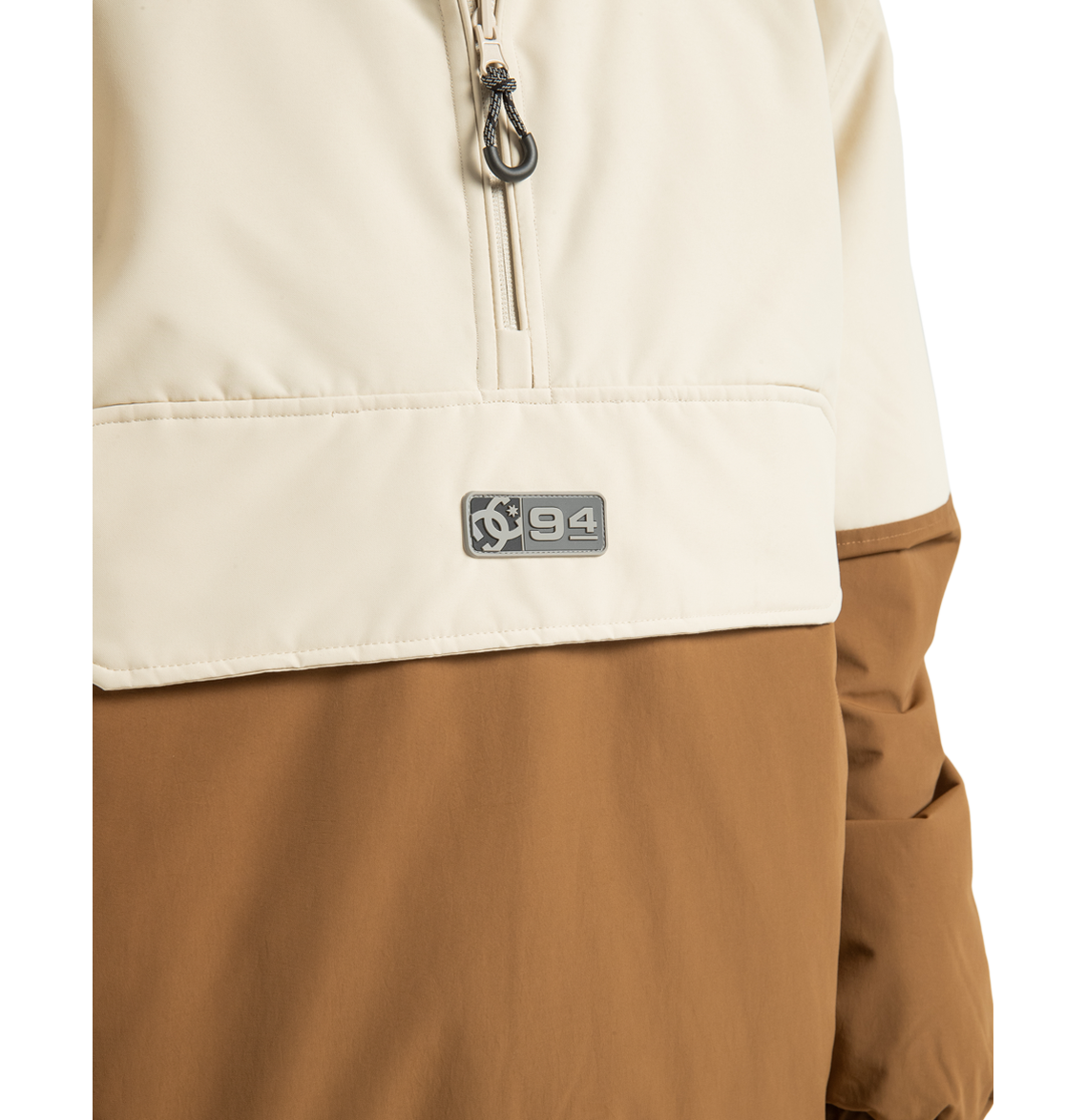 Close-up of the Unisex Nexus Reversible Insulated Anorak Jacket by DC Shoes, shown here in a cream and brown color-block design with a partial zipper and a small ‘94’ logo patch on the chest—ideal for your next outdoor adventure.