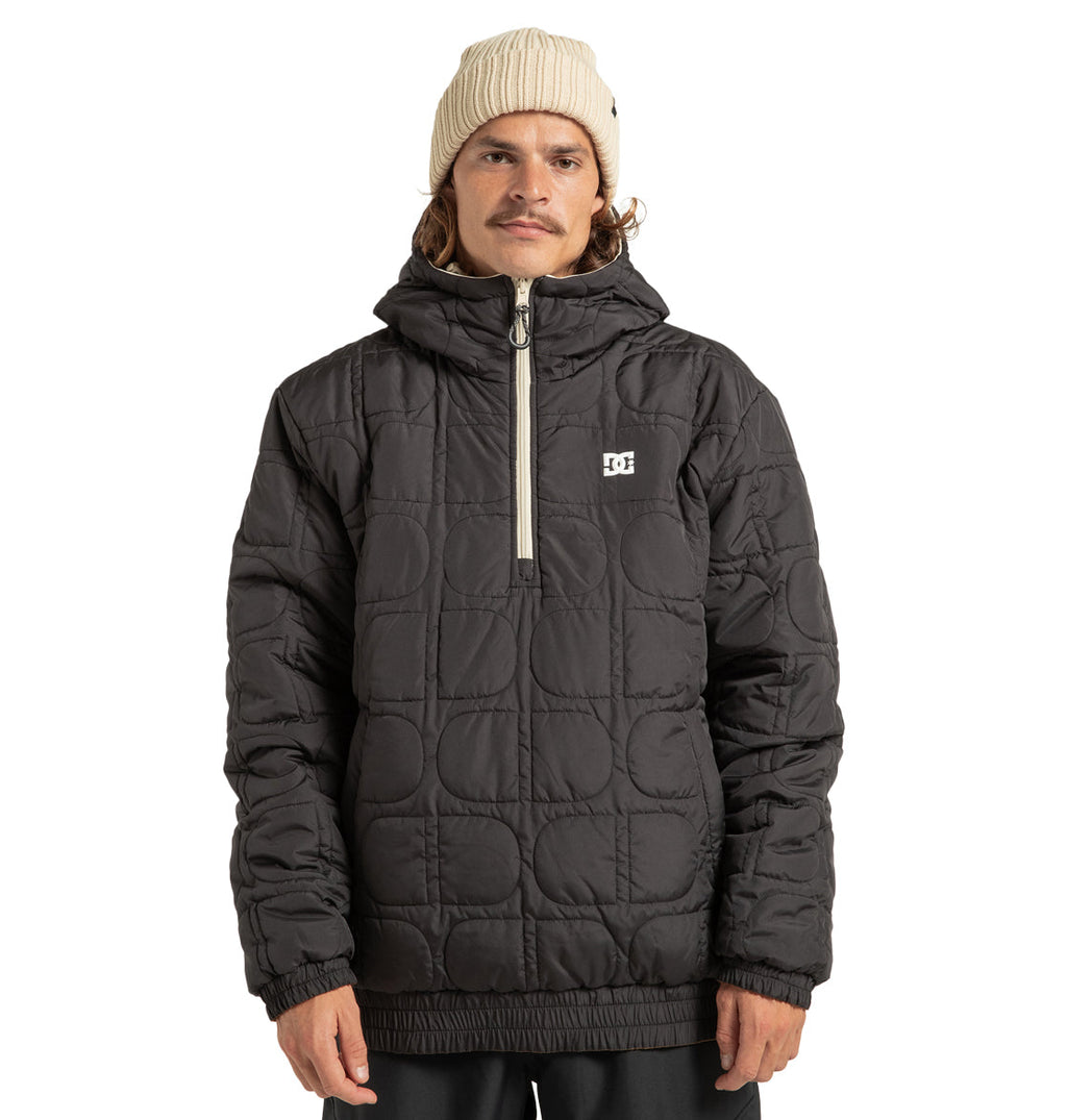 A person wearing a cream knit beanie and a black DC Shoes Unisex Nexus Reversible Insulated Anorak Jacket, featuring a partial front zipper and a small white logo on the chest, stands facing forward against a plain white background.