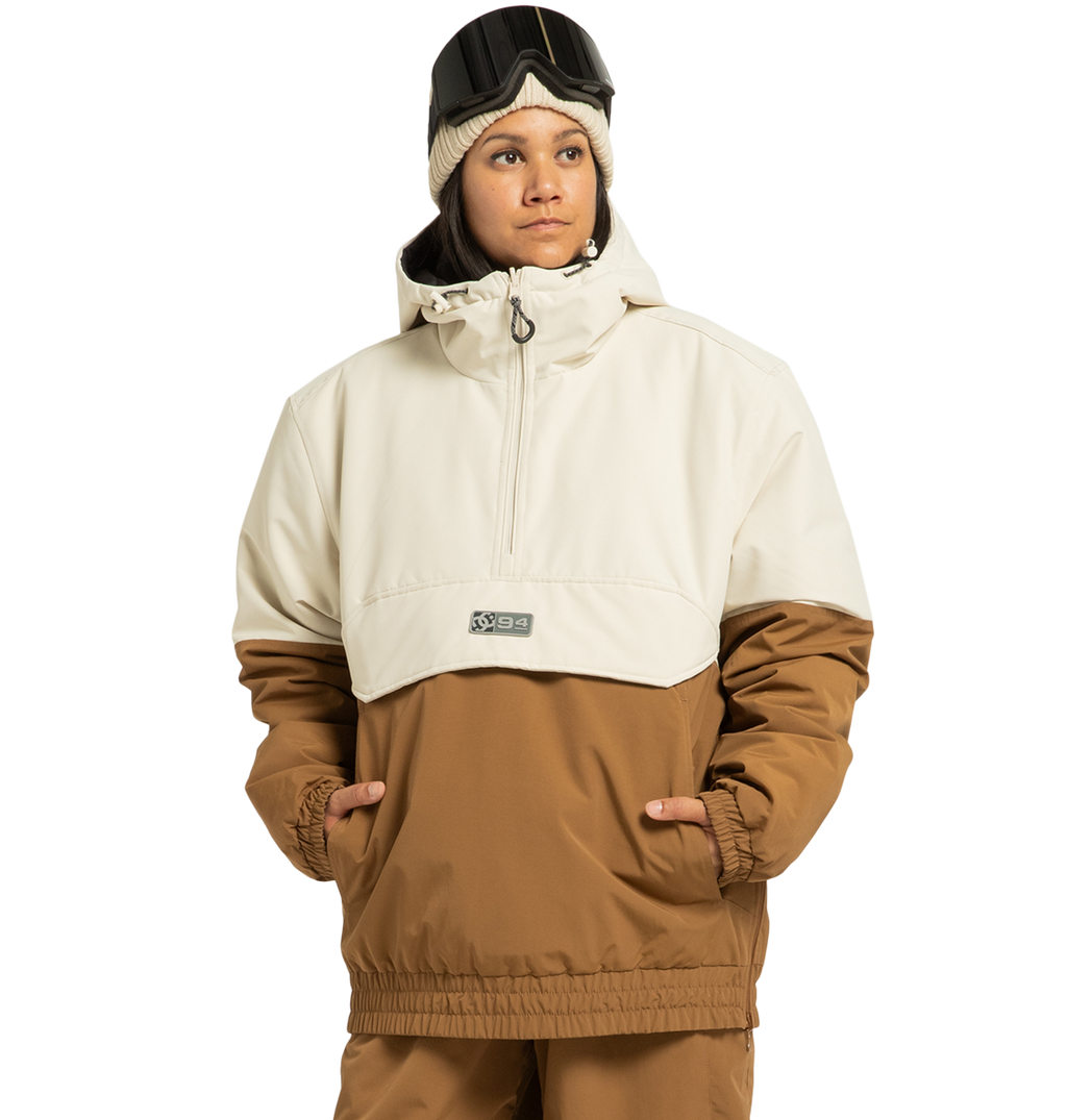 A person wearing the DC Shoes Unisex Nexus Reversible Insulated Anorak Jacket in beige and brown, paired with matching pants, a cream beanie, and ski goggles resting on their forehead, stands with hands in pockets against a plain white background—perfectly outfitted for any outdoor adventure.