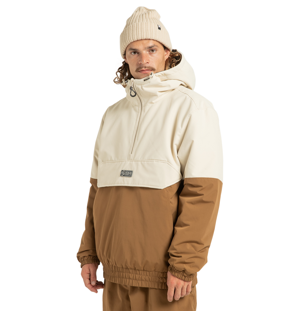 A person wearing a cream and brown DC Shoes Unisex Nexus Reversible Insulated Anorak Jacket made from recycled polyester, matching brown pants, and a cream knit beanie stands against a plain white background, looking at the camera with a neutral expression.