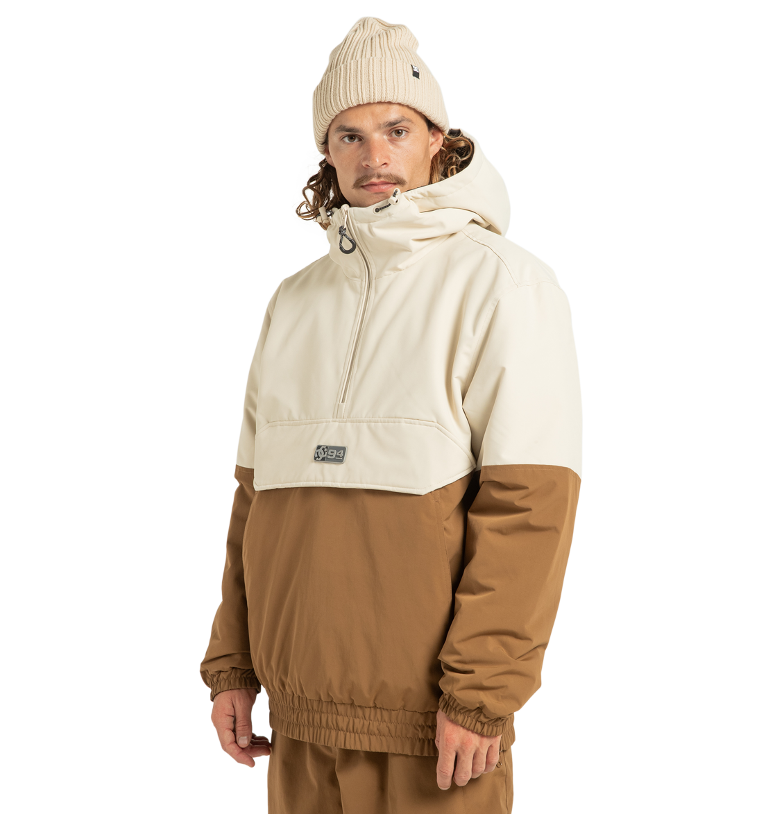 A person wearing a cream and brown DC Shoes Unisex Nexus Reversible Insulated Anorak Jacket made from recycled polyester, matching brown pants, and a cream knit beanie stands against a plain white background, looking at the camera with a neutral expression.