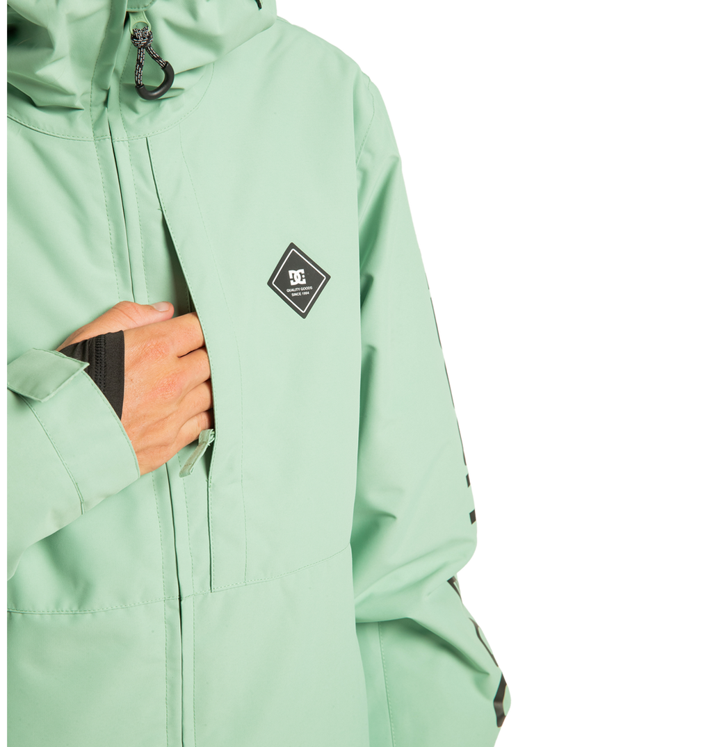 A person wearing the DC Shoes Unisex Basis Insulated Jacket in light green, featuring a diamond-shaped logo on the chest, puts their hand into one of the front zipper pockets. Crafted from recycled polyester, this stylish outerwear is ideal for winter activities. The photo captures the upper body against a white background.