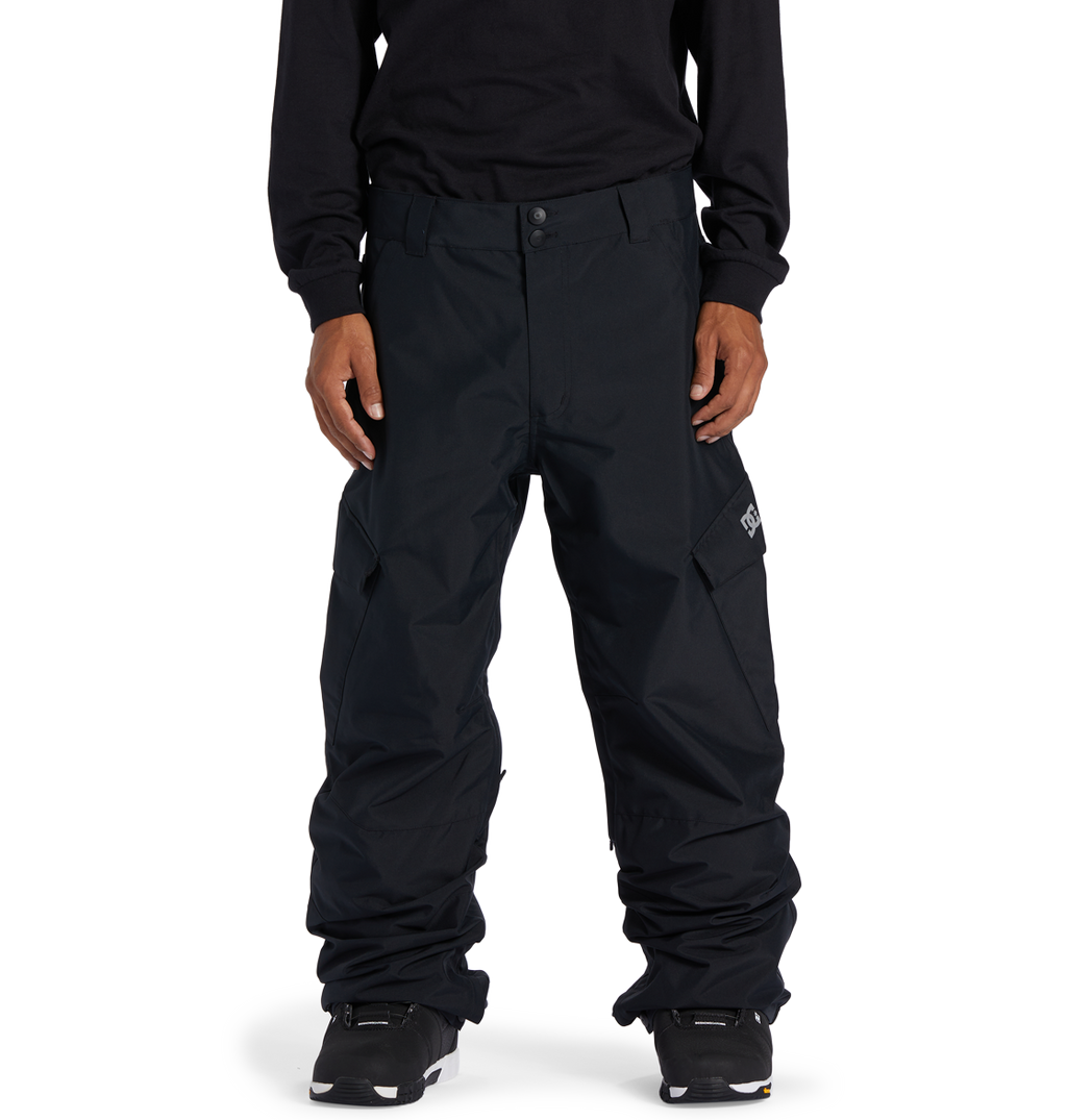 A person wearing loose-fitting DC Shoes Men’s Banshee Insulated Pants, a long-sleeve black shirt, and black sneakers stands facing forward against a white background, showcasing essential winter gear.