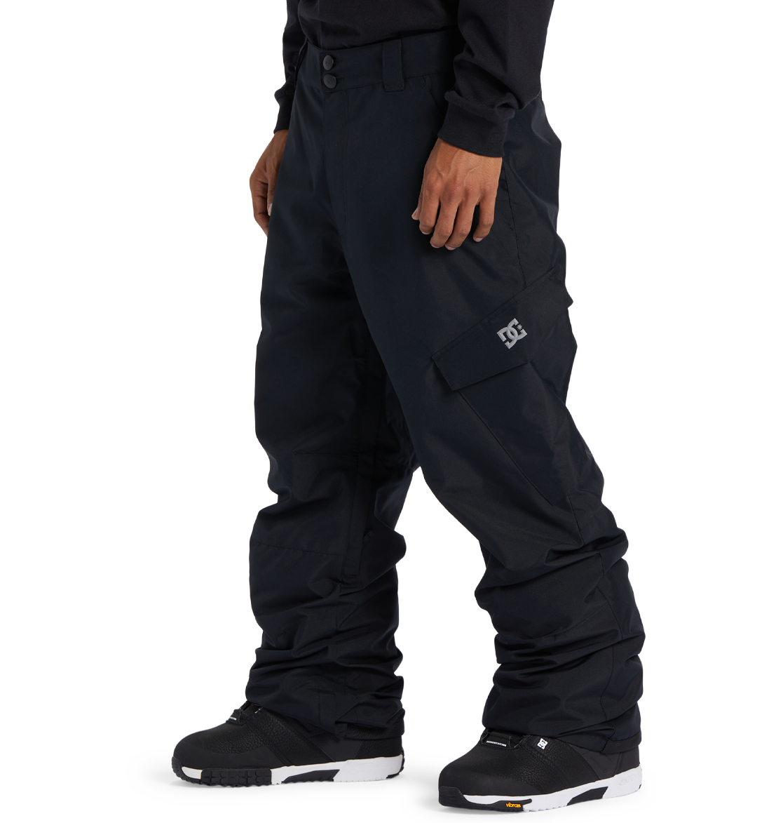 A person is wearing loose-fitting black DC Shoes Men’s Banshee Insulated Pants, featuring a cargo pocket and a white DC logo, paired with black snow boots, and standing against a plain white background. These pants are an essential piece of winter gear designed to provide added warmth and comfort on cold days.