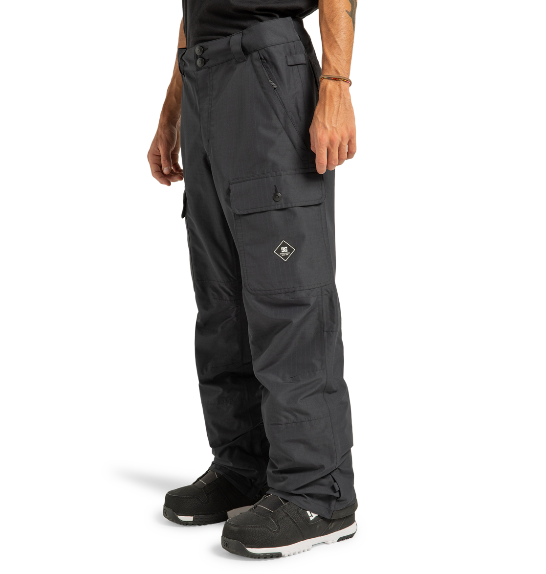 A person wearing DC Shoes Men’s Code Shell Pants in black, featuring eco-friendly materials and flap pockets, paired with black sneakers, stands against a plain white background.