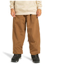 A person is standing against a plain white background, dressed in light brown DC Shoes Unisex Primo Shell Pants, a beige sweatshirt, and black sneakers. Renowned for their weather defense features, the Primo Shell Pants are a popular choice among outdoor enthusiasts. The image is cropped at the chest, leaving the person’s face out of view.