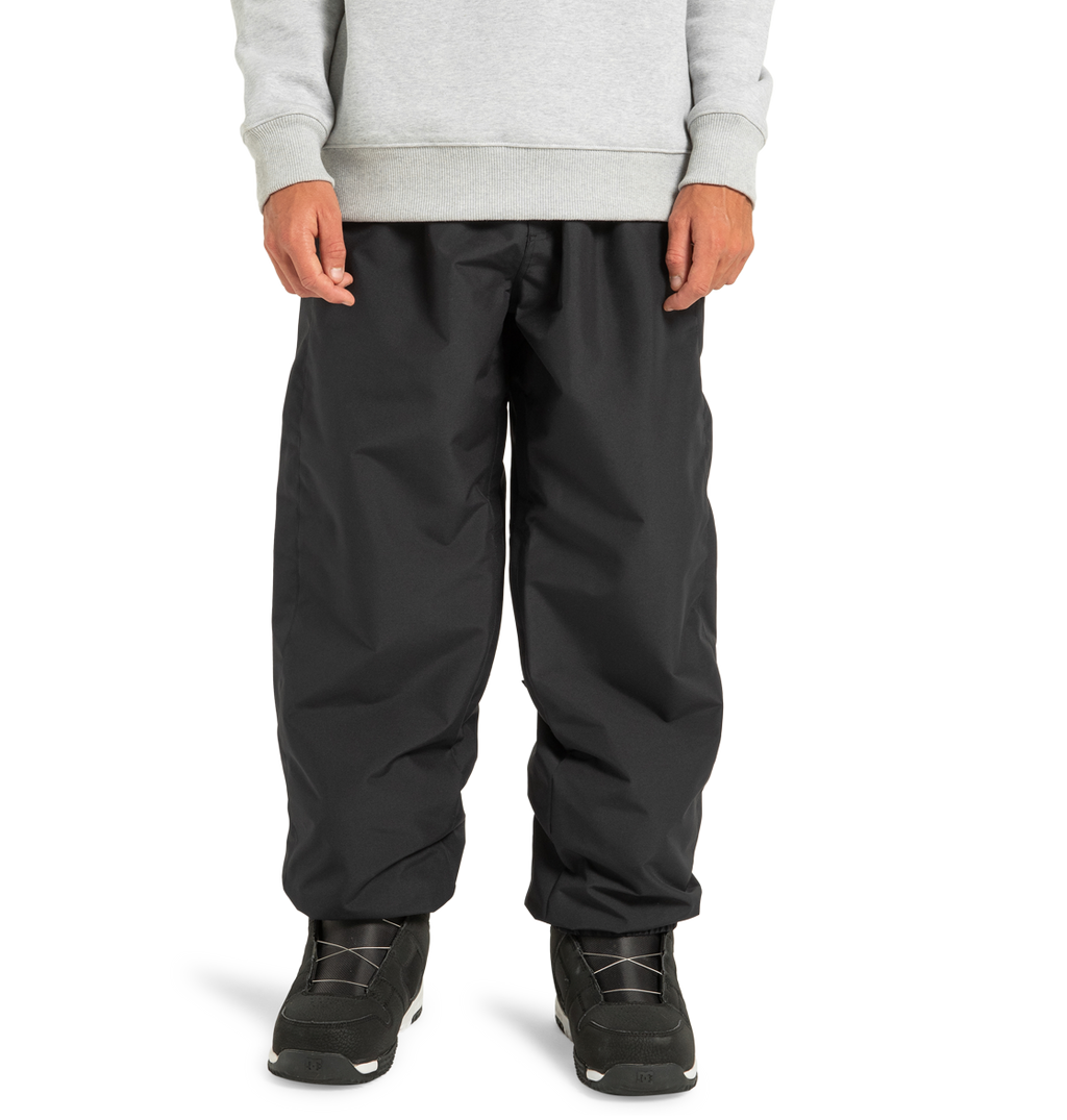 Model wearing DC Shoes Unisex Primo Snow Pants in black and a light gray sweatshirt, paired with black athletic shoes. Cropped below the shoulders, against a plain white background.