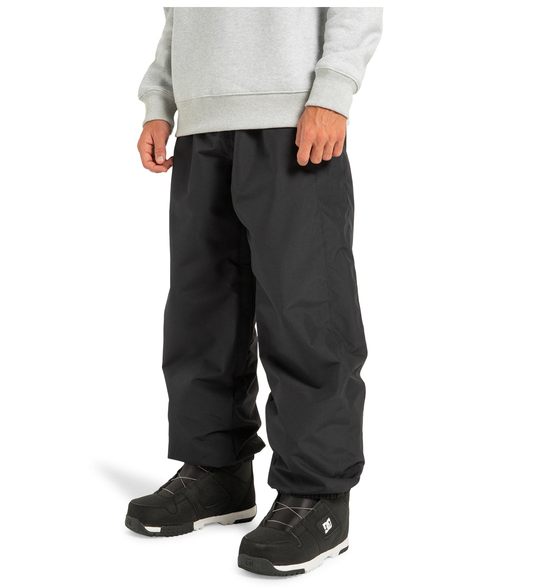 A person wearing a light gray sweatshirt, DC Shoes Unisex Primo Snow Pants in black made from recycled polyester, and black snow boots with white soles, standing against a plain white background.